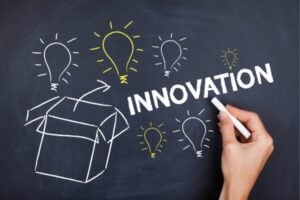 Hand sketching a box on a chalkboard with glowing light bulbs and the word INNOVATION.