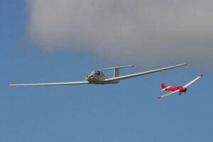 White glider being towed by a small red airplane in a blue sky with wispy clouds.