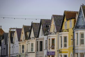 Row of pastel-colored gable-front houses along a seaside street with string lights overhead and a clear sky.